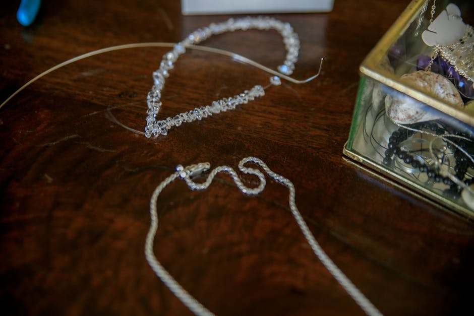 Close-up of elegant silver necklaces on a wooden table with a jewelry box.